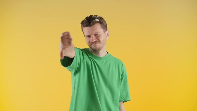 A man with stubble stands in front of the camera and gives a thumbs down. The man in the green t-shirt shakes his head and gives a thumbs down.