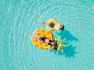 Aerial drone view of girls in swimming pool from above, happy kids swim on inflatable ring donut...