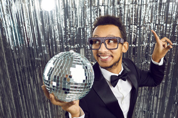 Lets get party. Cheerful young dark-skinned disco man in suit with shiny silver mirror disco ball...