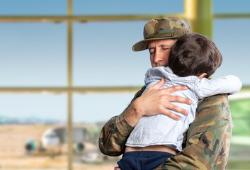Military father hugs his son when they are reunited after a mission with a blue sky in the background and copy space.
