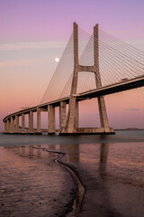 The Vasco da Gama Bridge in Lisbon, Portugal at sunset with moon. Cable-stayed bridge. Tagus river. Vertical shot. Long exposure.