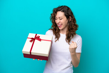 Young caucasian woman holding a gift isolated on blue background celebrating a victory
