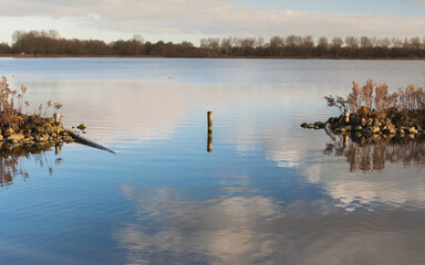 Fototapeta premium clouds reflecting in lake with rock barrier and treeline