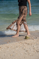 Young girl walking at the beach in summer vacation. Stylish happy woman wears in leopard pant having fun on the tropical beach with copy space. Close up of legs with waves.