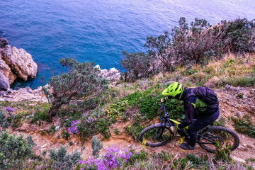 Unrecognisable mountain biker descends on a challenging trail steep towards the sea, Finale Ligure,...