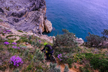 Unrecognisable mountain biker descends on a challenging trail steep towards the sea, Finale Ligure, Italy