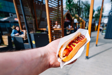 man holds fresh hot dog with sauce in hands. Street food, fast food outdoor