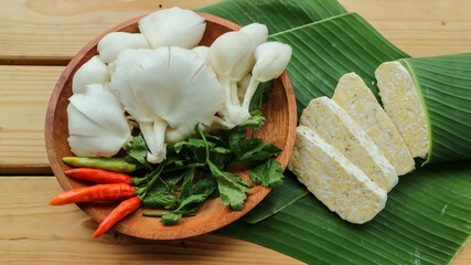 Tempe slices, oyster mushroom, chili on a wooden plate. Tempeh or Tempe is an Indonesian specialty. Vegetarian food.