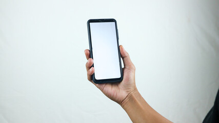 Asian man holding big smartphone with white, red, green, blue blank screen in hand, showing close to camera and pointing at device. Gadget with empty free space for mock up, banner