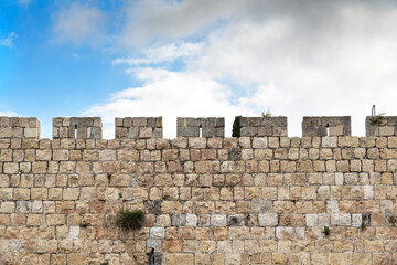 Fototapeta na wymiar Background with fragment of the upper part of the fortress wall of Jerusalem Old City with the blue sky and clouds on the background