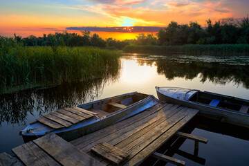 Evening landscape with an old rustic wooden pier and old boats at sunset on the Dnieper Delta
