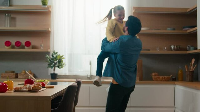 Happy family at kitchen blurry view little daughter run to dad child kid girl running to father daddy rise up baby spinning around swirling hugging cuddling touch noses bonding affection childcare