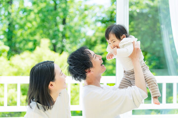 Fototapeta premium 新緑の前で赤ちゃんを高い高いする両親