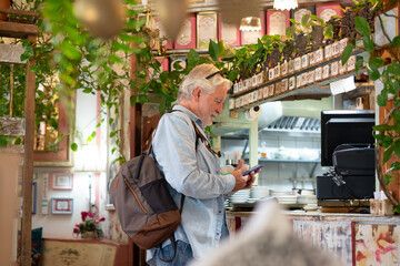 Senior white-haired man pays at the coffee shop checkout using the application on his mobile phone. Concept of modernity and online electronic payments