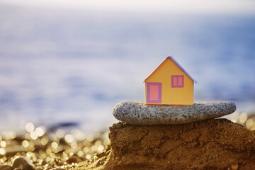 Fototapeta na wymiar a small paper house against the backdrop of the sea at sunset, the concept of real estate services, a dream of a house by the se