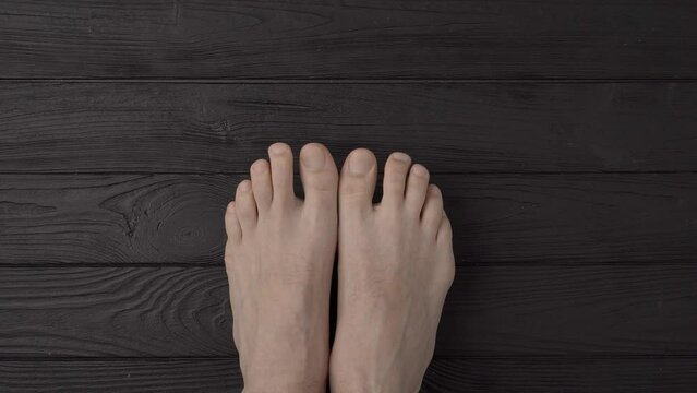Male feet with well-groomed trimmed nails on a black wooden background or floor. Close up, top view, point of view
