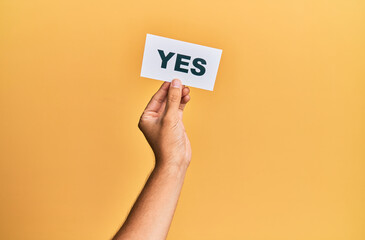 Hand of caucasian man holding paper with yes word over isolated yellow background