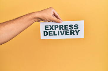 Hand of caucasian man holding paper with delivery express message over isolated yellow background