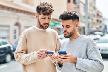 Young couple using smartphone and credit card standing together at street