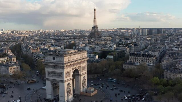 Aerial above Arc de Triumph in foreground and Eifel Tower in background, Paris. Late afternoon light, historical building rooftops