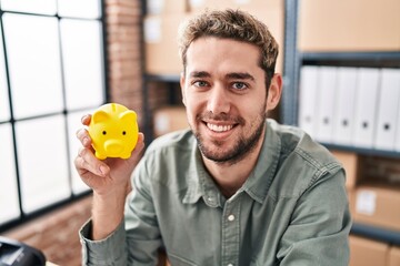 Young man ecommerce business worker holding piggy bank at office