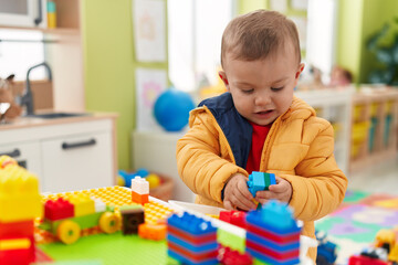 Adorable blond toddler playing with construction blocks standing at kindergarten