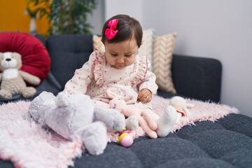 Fototapeta premium Adorable hispanic baby playing with doll sitting on sofa at home