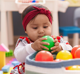 Fototapeta na wymiar Adorable hispanic baby playing with balls sitting on floor at kindergarten