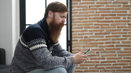 Obraz premium Young redhead man using smartphone with serious expression at home