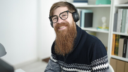 Naklejka premium Young redhead man student using computer and headphones studying at library university
