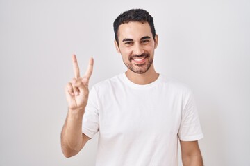 Fototapeta premium Handsome hispanic man standing over white background showing and pointing up with fingers number two while smiling confident and happy.