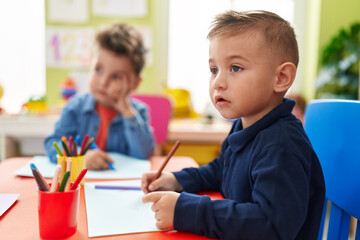 Adorable boys preschool students sitting on table drawing on paper at kindergarten