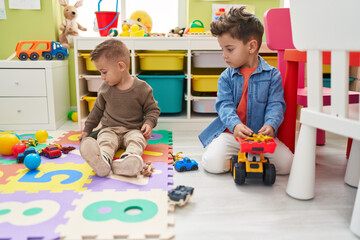 Adorable boys playing with cars toy and tractor sitting on floor at kindergarten