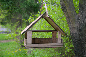Fototapeta na wymiar A birdhouse shaped like a cozy little house hangs on a tree, providing a welcoming shelter for birds in the park during spring .