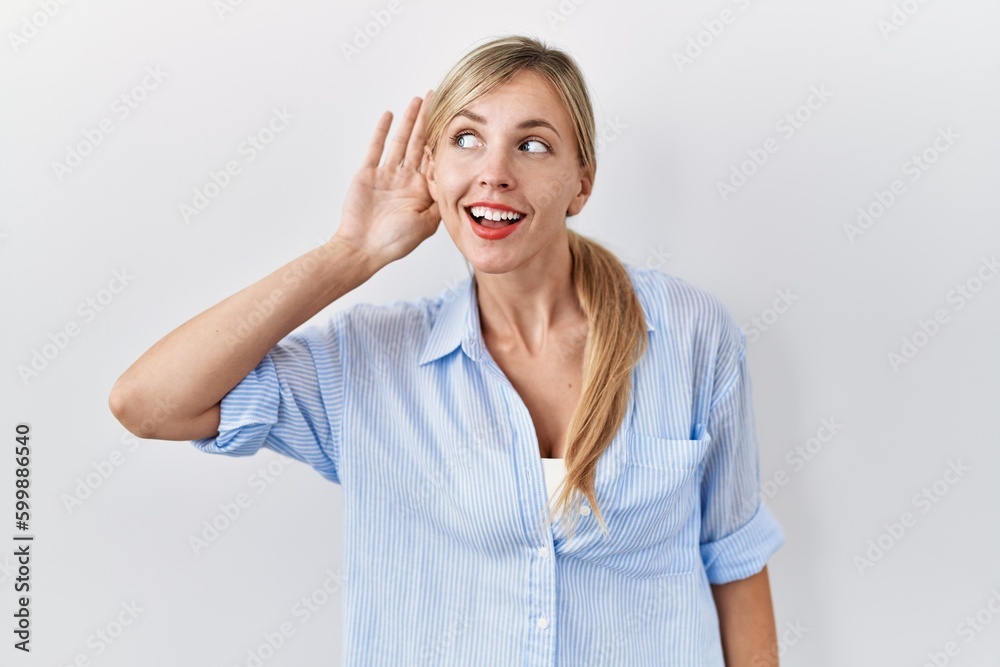 Sticker Beautiful blonde woman standing over white background smiling with hand over ear listening an hearing to rumor or gossip. deafness concept.