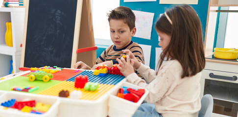 Adorable boy and girl playing with construction blocks sitting on table at kindergarten
