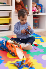 Adorable hispanic boy playing with car and dinosaur toy sitting on floor at kindergarten