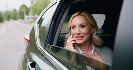 Fototapeta na wymiar Beautiful adult caucasian woman rides on rear passenger seat of car, looking wonder out of the window during important phone call