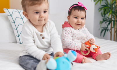 Adorable boy and girl sitting on bed playing with toys at bedroom