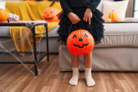 Adorable hispanic girl having halloween party holding pumpkin basket at home