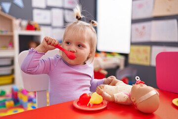 Adorable blonde girl playing to eat sitting on table at kindergarten