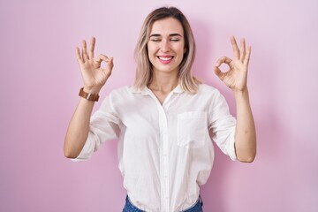 Young beautiful woman standing over pink background relaxed and smiling with eyes closed doing meditation gesture with fingers. yoga concept.