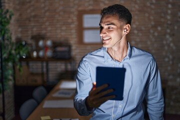 Handsome hispanic man working at the office at night looking away to side with smile on face, natural expression. laughing confident.