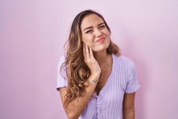 Fototapeta premium Young hispanic woman standing over pink background touching mouth with hand with painful expression because of toothache or dental illness on teeth. dentist