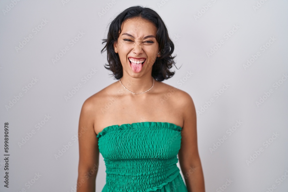 Sticker young hispanic woman standing over isolated background sticking tongue out happy with funny expressi