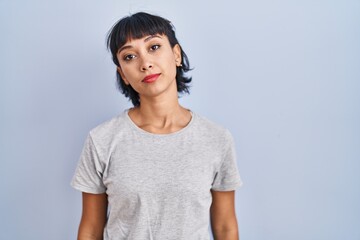 Fototapeta premium Young hispanic woman wearing casual t shirt over blue background relaxed with serious expression on face. simple and natural looking at the camera.