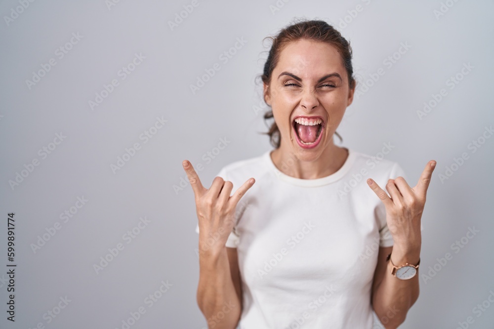 Sticker Beautiful brunette woman standing over isolated background shouting with crazy expression doing rock symbol with hands up. music star. heavy music concept.