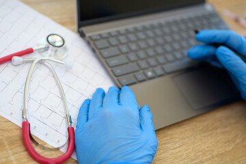 Laptop, stetoskop i dłonie w rękawiczkach na biurku