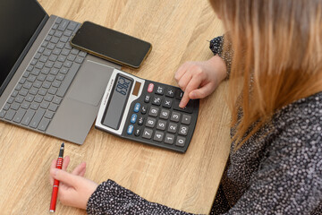 Kobieta licząca na kalkulatorze siedząca przy biurku - obrazy, fototapety, plakaty
