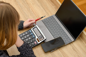 Kobieta licząca na kalkulatorze przy biurku - obrazy, fototapety, plakaty